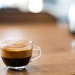 A close-up shot of freshly brewed espresso in a glass cup on a wooden table.